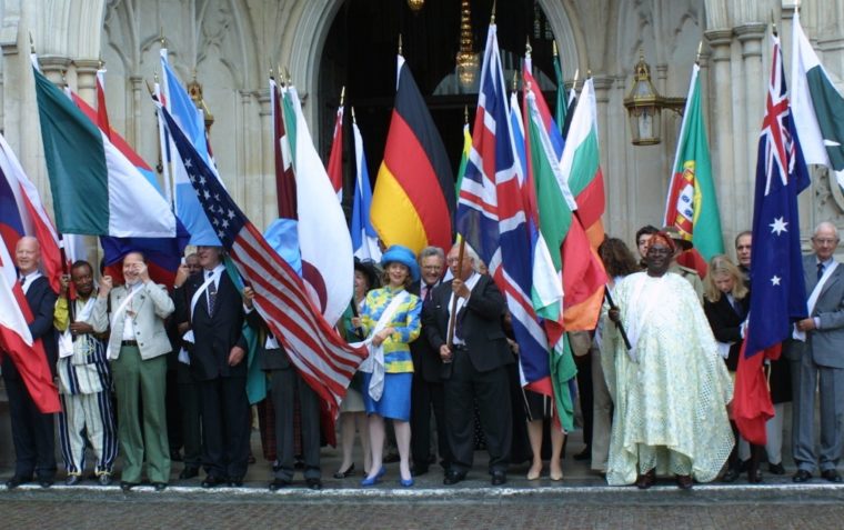 A group of international representatives standing in front of a building and holding their country flags.