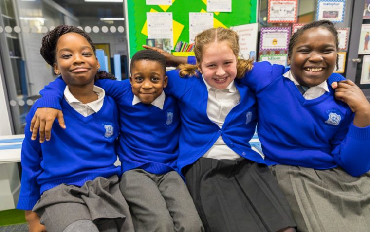 Team shot of primary school children (three girls and a boy) smiling with linked shoulders