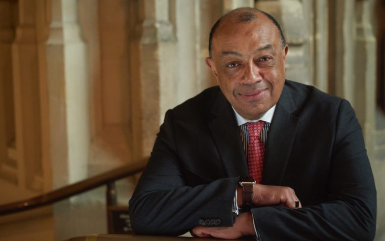 Paul Boateng close up with columns of Parliament behind him