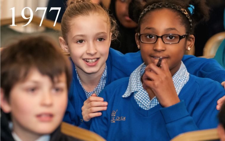 Three primary school pupils (two girls and a boy) sitting inside a classroom.