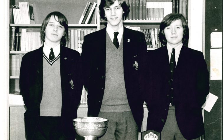 A picture of the young Michael Crick (left) and his winning team in 1975 standing behind a table with their trophies on it.