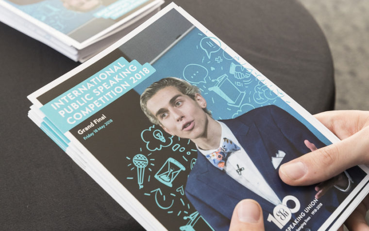 A photo of someone holding multiple copies of the International Public Speaking Competition 2018 edition