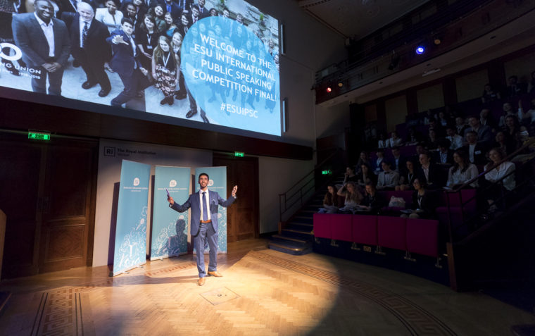 Kamal delivering his speech at the International Public Speaking Competition with the dramatic light being shinned on him