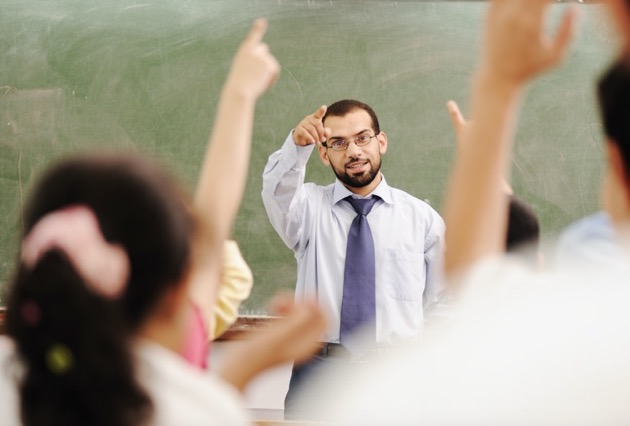 Someone picking a pupil to answer his question with many students raising their hands to answer