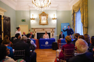 Photo of a debating event with one speaker delivering their speech while another is standing up to ask them a question