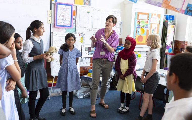 All girls primary school pupils standing inside a classroom and listening to the tutor speaks.