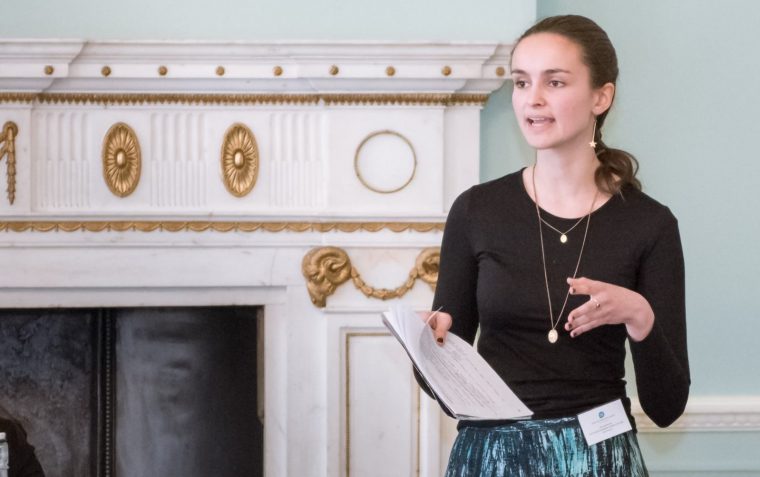 A picture of a young female debater standing in front of a fireplace inside the ESU London's office building at Dartmouth House.