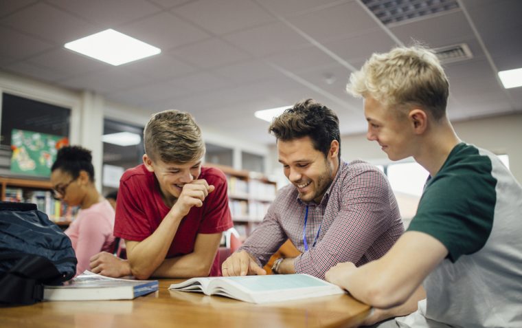3 people sitting in a library and reading a book while laughing