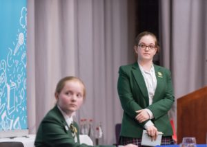 Two pupils looking at another pupil giving a speech (who is not in the picture)