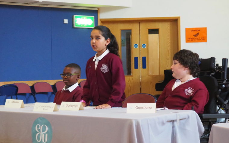 A student, in the role of the chairperson, delivering her remarks while her teams mates watch and listen to her carefully