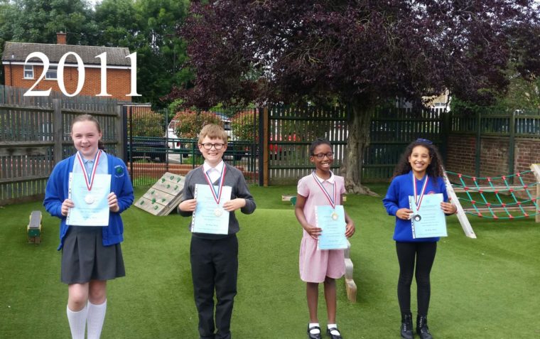 Four primary school pupils (a boy and three girls) showcasing their certificates outside in the school garden.