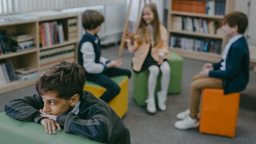 A lonely child stands on his own away from a group of other children talking