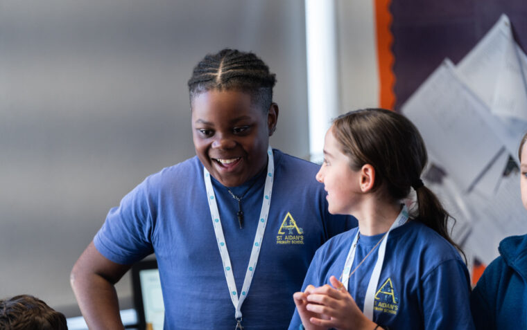 Two young students in a classroom talking with each other, smiling.