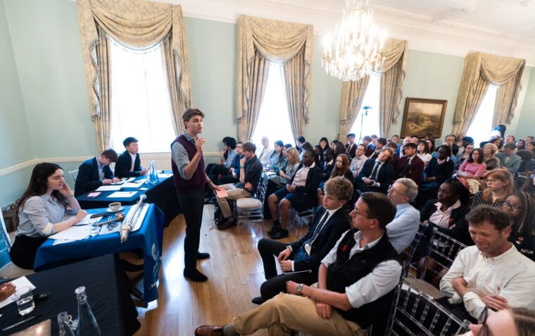A young man stood in front of a room of people presenting