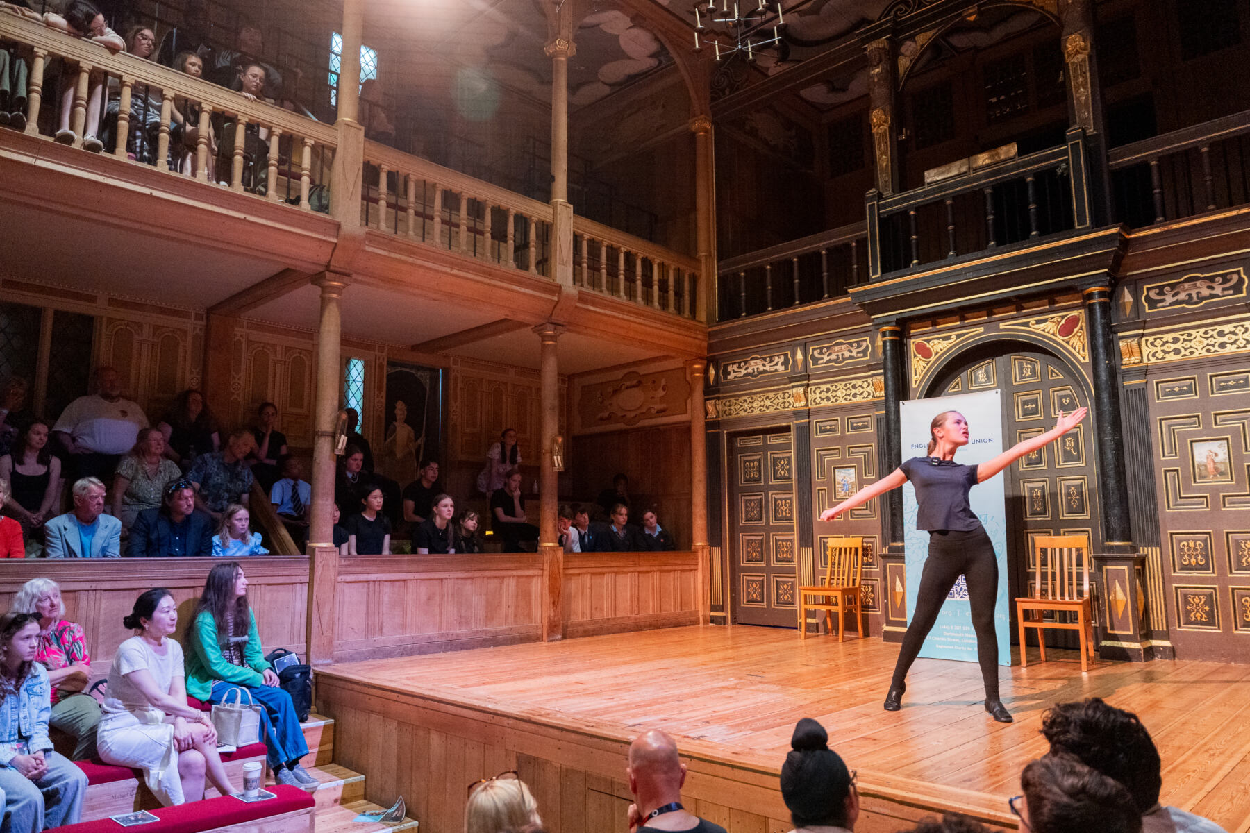 young girl on a stage performing passionately with her arms open, in front of an audience
