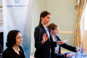 Young lady with dark hair speaking passionately, surrounded by her two teammates