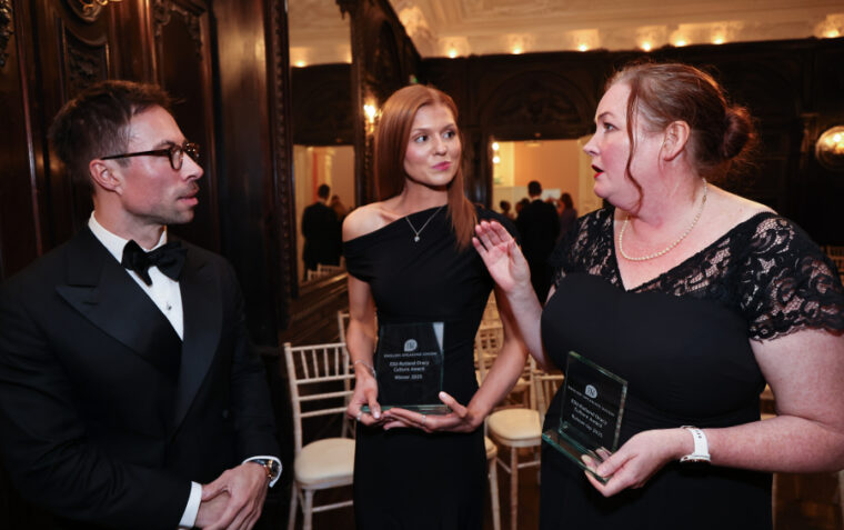 Two women holding awards talking to a man