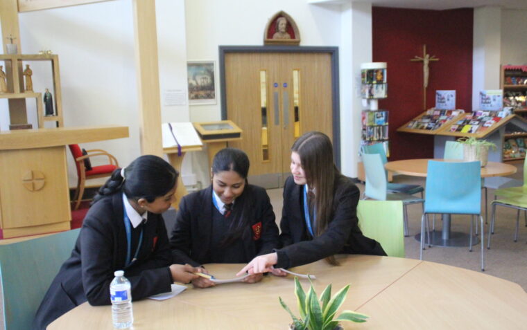 Three schoolgirls sat at a table, discussing their work